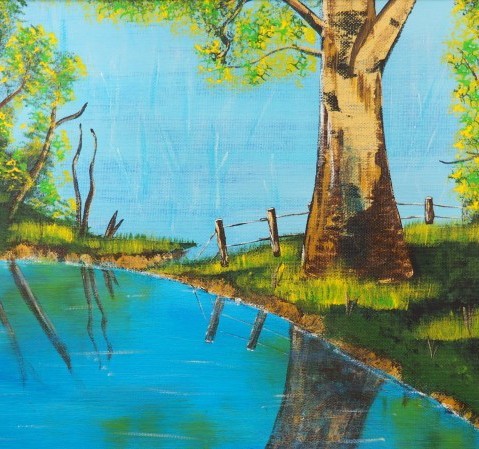 Tree on a green riverbank next to a blue river