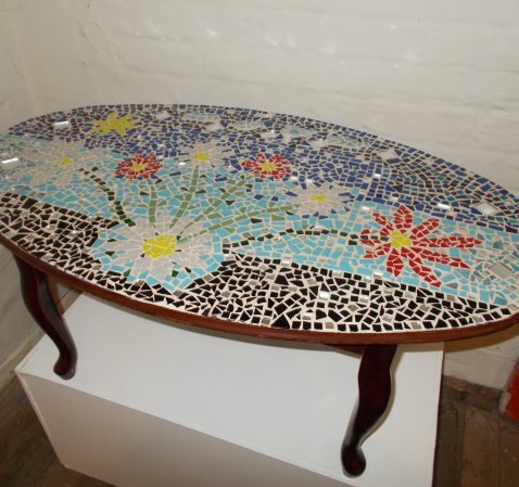 A table with a coloured mosaic top in a flower design, on a white plinth 