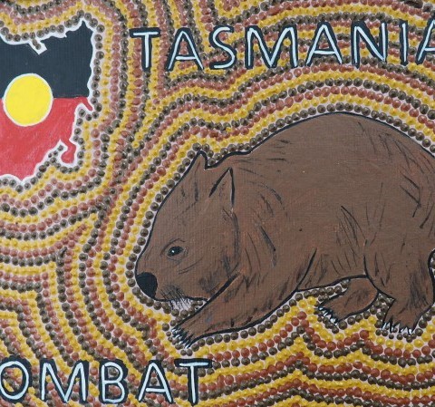 A brown wombat on a dot painting background, with a Tasmanian map in colours of the Aboriginal flag and the words Tasmanian Wombat