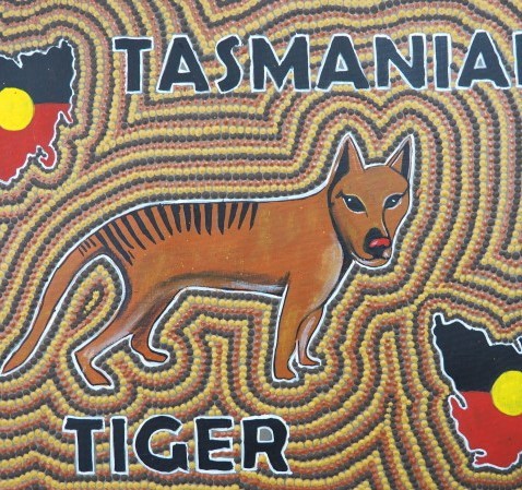 Brown Tasmanian Tiger on a dot painting background, with two maps of Tasmania in the colours of the Aboriginal flag, and the words Tasmanian Tiger
