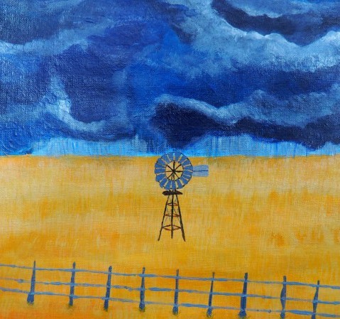A steel windmill standing on a yellow field behind a wire fence, under a stormy sky