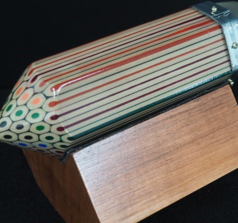 Wooden sculpture of a giant, coloured pencil made of many smaller pencils, resting on a wooden block