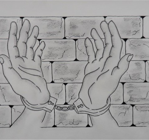 Black and white image of two hands handcuffed together, in front of a brick wall