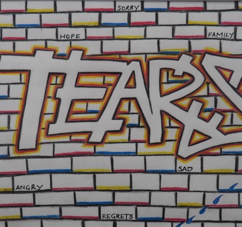 White brick wall with the bricks outlines in colour, and the word Tears