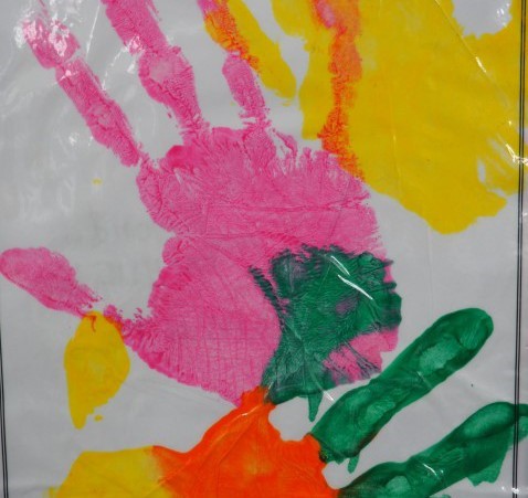 Three children's hand prints in pink, yellow and green